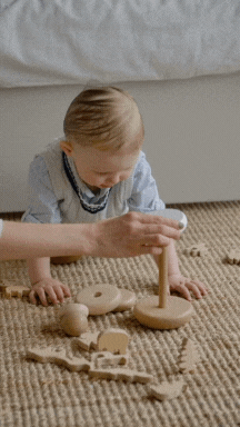 Bebé explorando un juguete de madera con la guía de un adulto